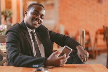 Restoranda gülümseyen ve mutlu bir şekilde akıllı telefon kullanan Afrikalı iş adamı.