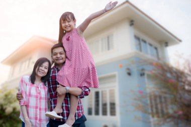Mutlu Asyalı bir ailenin gülümseyerek evinin yanında durması ve sarılmaları.