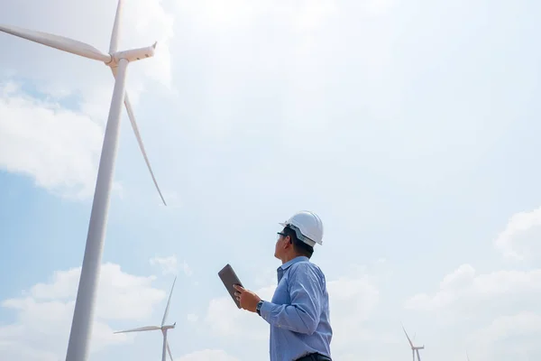 Engineer windmills working on tablet PC with the wind turbine in background