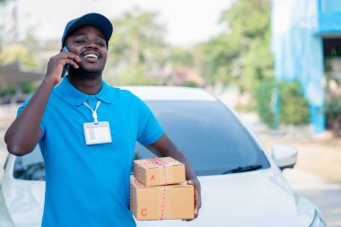 Afrikalı erkek posta kuryesi elinde teslimat paketleri olan akıllı telefonlu bir adam.