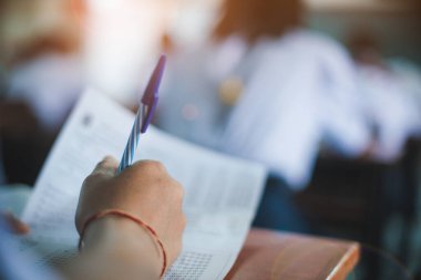 Öğrencinin eli, eğitim sınavı konsepti için sınava giriyor ve sınıfta cevap yazıyor.