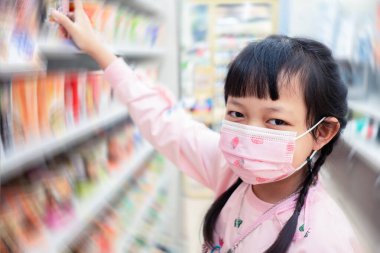 Covid-19 ya da süpermarkette Corona virüsünü korumak için ağzı kapalı tutmak için yüz maskesi takan Asyalı küçük kız çocuğu.