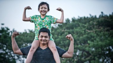 Asyalı küçük kız babasının omuzlarında oturuyor ve hareketlerini gülümseme ve mutlulukla güçlü kılıyor. Babalar günü kavramı.