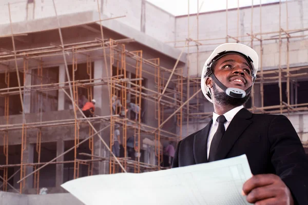 African site contractor engineer with hard hat holding blue print paper with building in background