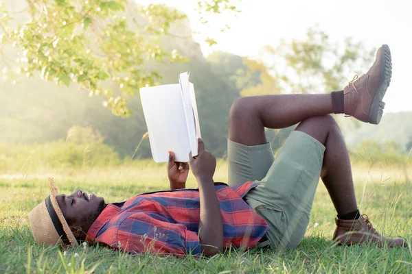 African man reading a book on the grass happily on vacation