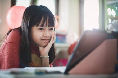 Asyalı küçük kız evde online dersi sırasında gülümsüyor ve mutlu, karantina sırasındaki sosyal uzaklık, online eğitim konsepti