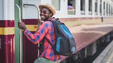 Şapkalı ve sırt çantalı Afrikalı gezgin tren istasyonuna gidiyor. Macera seyahati konsepti.