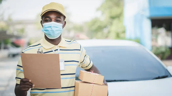 African delivery man with face mask holding a box package and cardboard.Concept of quarantine delivery service