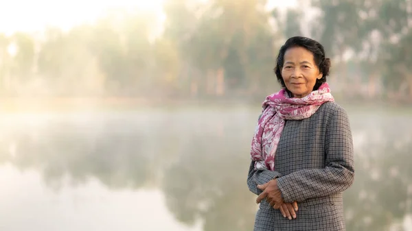 Happy asian elderly senior smile with the nature lake in background, Lifestyle of Asian old women concept