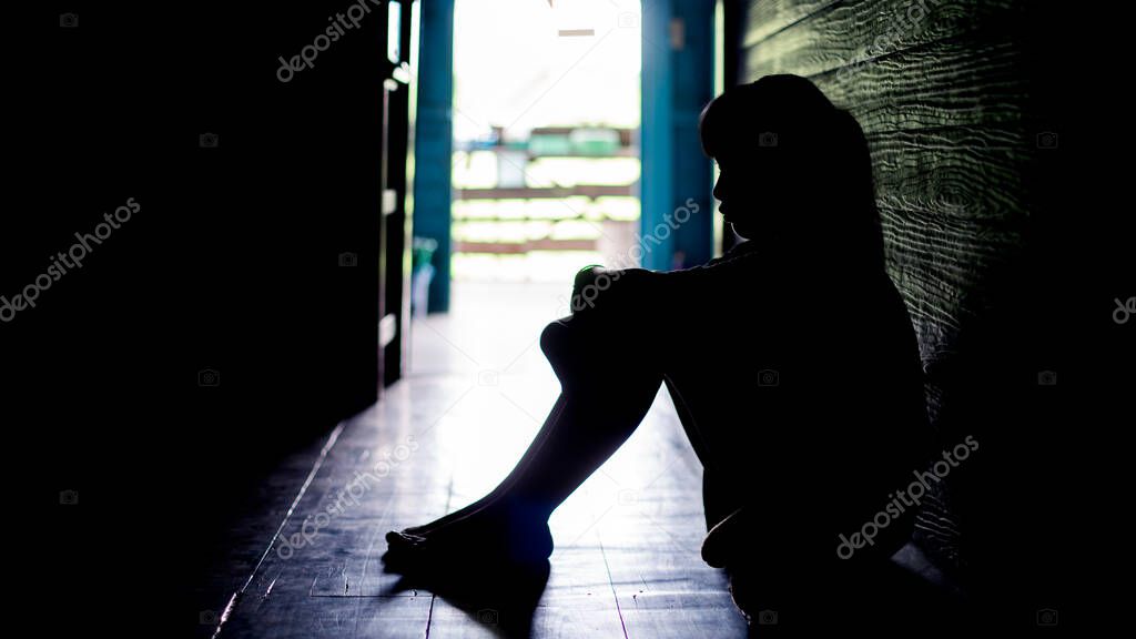 Sad lonely little girl crying while sitting on the floor in  dark room with an attitude of sadness.Concept of depression or domestic violence child