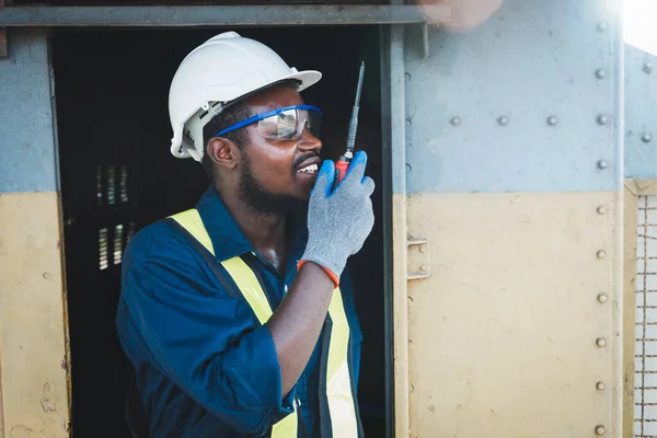 Afrikalı mühendis radyo iletişimi veya telsizle konuşurken kazaları önlemek için güvenlik gözlüğü, kask ve eldiven takıyor