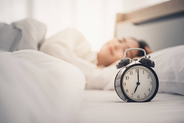 Young woman sleeping on bed with alarm clock in morning.