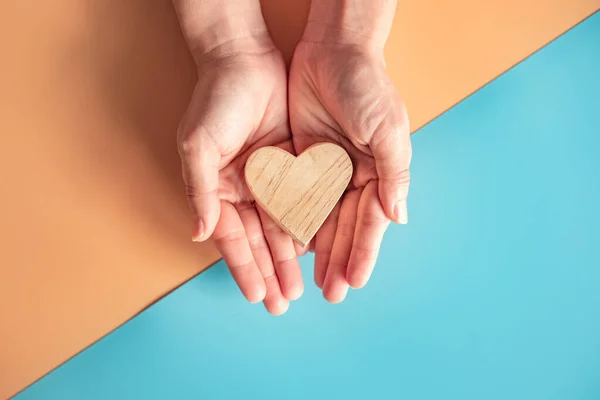 Manos Sosteniendo Corazón Madera Sobre Fondo Papel Color Azul Naranja —  Fotos de Stock