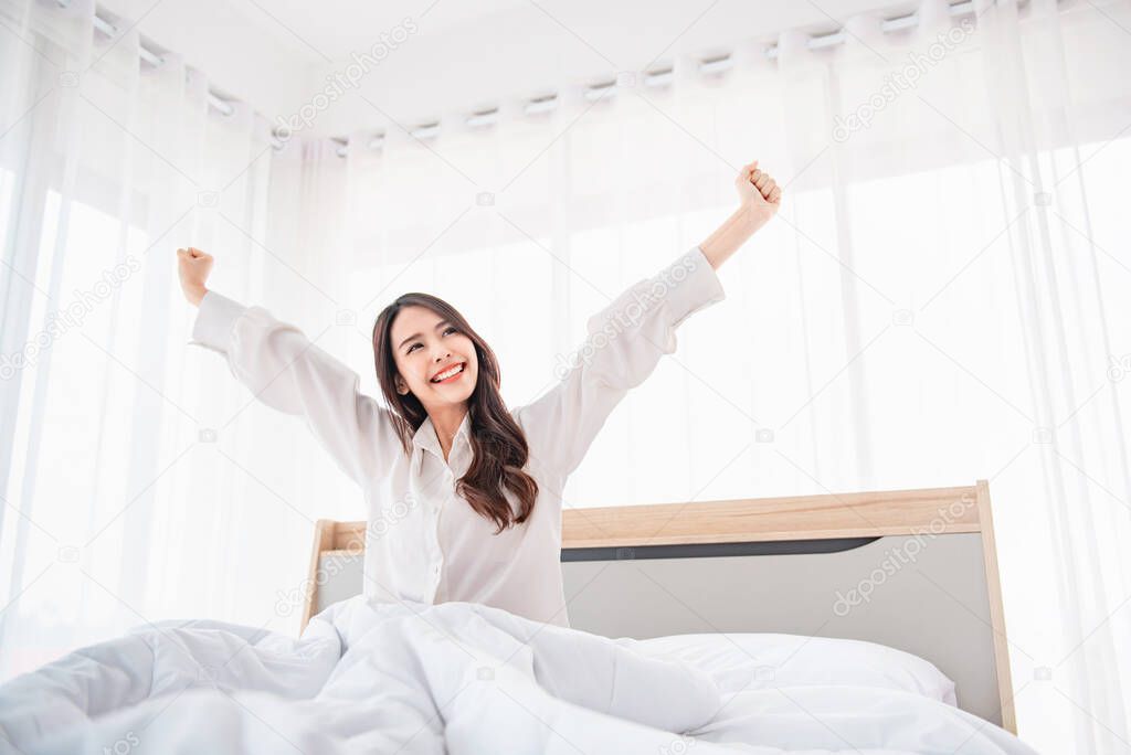 Happy asian woman stretching hands in bed after wake up in the morning, Concept of a new day and joyful weekend.