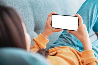 Oturma odasındaki kanepede boş beyaz ekranlı cep telefonu kullanan kadın, boşluğu kopyala.