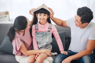 Mutlu Asyalı aile (anne, baba, çocuk kız) okula gitmeden önce gülümserken birlikte oynuyorlar.