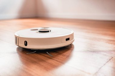 Beyaz robotik süpürge, evdeki plastik zeminde toz temizliyor.