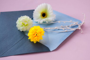 Pembe arka planda mavi bir zarfın içinde çiçekler.