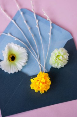 Pembe arka planda mavi bir zarfın içinde çiçekler.