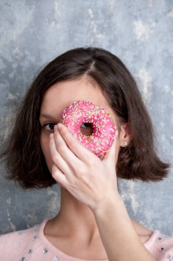 Pembe bluzlu bir kız elinde bir donut tutuyor. Gözünün yanına yakın.