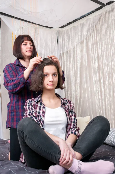 A woman twists a girl\'s hair into curlers at home on the bed