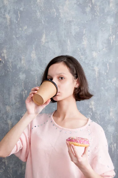 ブルネットの女の子持っていますAドーナツで彼女の手と飲み物のコーヒー — ストック写真