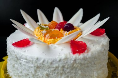 Siyah arka planda taç yaprakları ve jölelerle süslenmiş beyaz pasta.