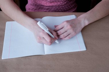 Pembe bluzlu bir kız kalemle deftere yazıyor.