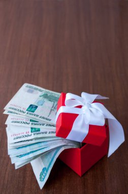 Masanın üzerinde kırmızı bir hediye kutusu var. Beyaz bir fiyonk ve 1000 ruble değerinde Rus rublesi.