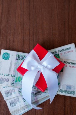 Masanın üzerinde kırmızı bir kutu var. Üzerinde beyaz bir fiyonk var. Bin ruble değerinde Rus rublesi.