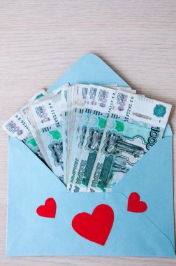 Masanın üzerinde mavi bir zarf var. Üzerinde Rus banknotları ve 1000 ruble değerinde kalpler var.