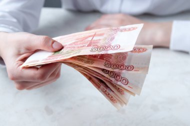 Bir kadının eli masanın üzerinde beş bin ruble tomar para tutuyor.