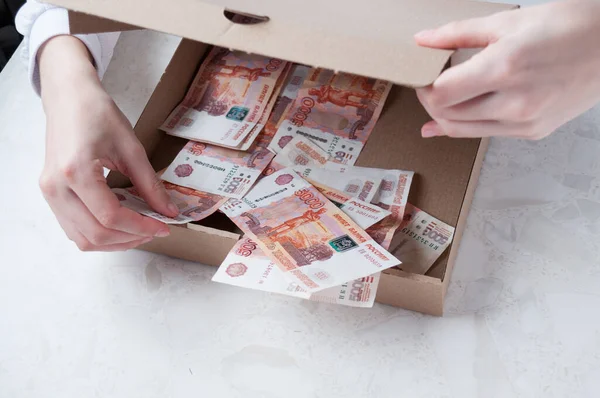 A woman\'s hand pulls out from a cardboard box five thousand rubles, the concept of profit from the sale of pizza