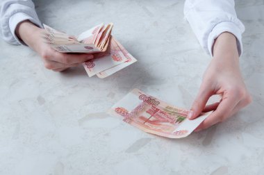 Masadaki beyaz gömlekli bir kız para sayıyor, bir banka çalışanı.