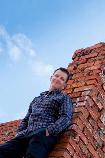 İnşaat halindeki bir evin duvarının arkasında duran genç bir adamın portresi.