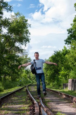 Sırt çantalı bir adam yazın ormanda demiryolu boyunca yürür.