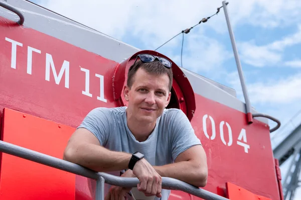 Bir adam kırmızı bir lokomotifin arka platformunda duruyor.