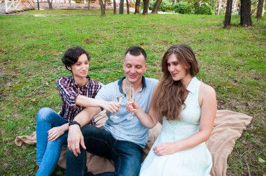 Pikniğe giden üç arkadaş yazın çimenlerde dinlenir, bardakta şarap içerler.