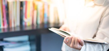 Not ya da yorum için uzay kitabıyla el ele tutuşan ve sosyal uzaklık kavramı ile Covid-19 'u korumak için kütüphanede oturan bir kadın..