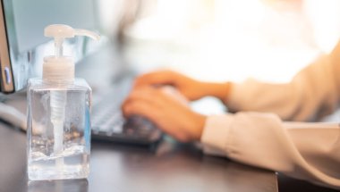 Önleyici Covid-19 ve korunma için bilgisayarın yanına koyulan bilgisayar laptor ve alkol jeli ile birlikte klavye yazan kadın. Yeni normal ve sosyal mesafeleme kavramı için ortak çalışma alanında çalışmak.