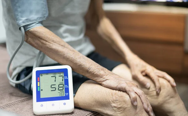 Yaşlı adam tansiyon monitörünü ve kalp atış hızı monitörünü dijital basınç göstergesiyle kontrol ediyor. Tıbbi ve sağlıklı konsept.