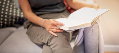 Kadın, evinde, oturma odasındaki kanepede otururken rahatlamak için defter ve kitap okuyor..