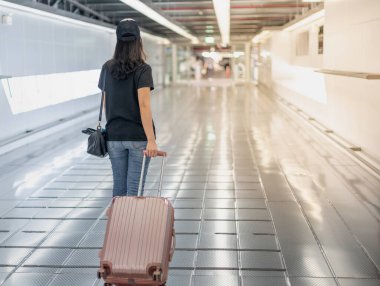 Bavul taşıyan ve cerrahi maske takan Asyalı bir kadın havaalanından bilet almak için giriş yapmaya hazırlanıyor. Covid-19 salgını sırasında. 