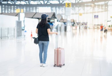 Bavul taşıyan ve cerrahi maske takan Asyalı bir kadın havaalanından bilet almak için giriş yapmaya hazırlanıyor. Covid-19 salgını sırasında. 