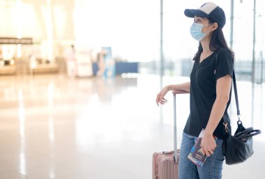 Bavul taşıyan ve cerrahi maske takan Asyalı bir kadın havaalanından bilet almak için giriş yapmaya hazırlanıyor. Covid-19 salgını sırasında. 