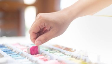 Masaya koyulan kutuda canlı pembe iplikler ve farklı renkler tutan terzi kadının ellerini kapatın ve beyaz pamuk ve çerçeve ahşap kullanmaya hazırlanın. Hobi ve eğlence konsepti için..