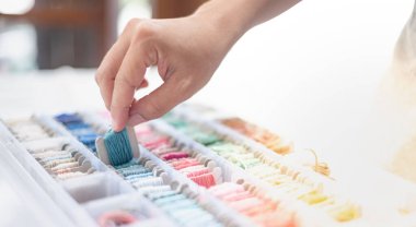 Okyanus mavisi iplikleri tutan terzi kadının ellerini kapatın ve masaya koyduğunuz kutuda farklı renkler olsun ve beyaz pamuk ve çerçeve ahşap kullanmaya hazır olun. Hobi ve eğlence konsepti için..