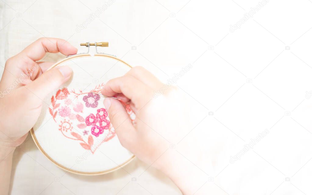 Female hand holding wood embroidery frame and needle working on pattern stitching in a process of handiwork.  Enjoying leisure time on weekends.