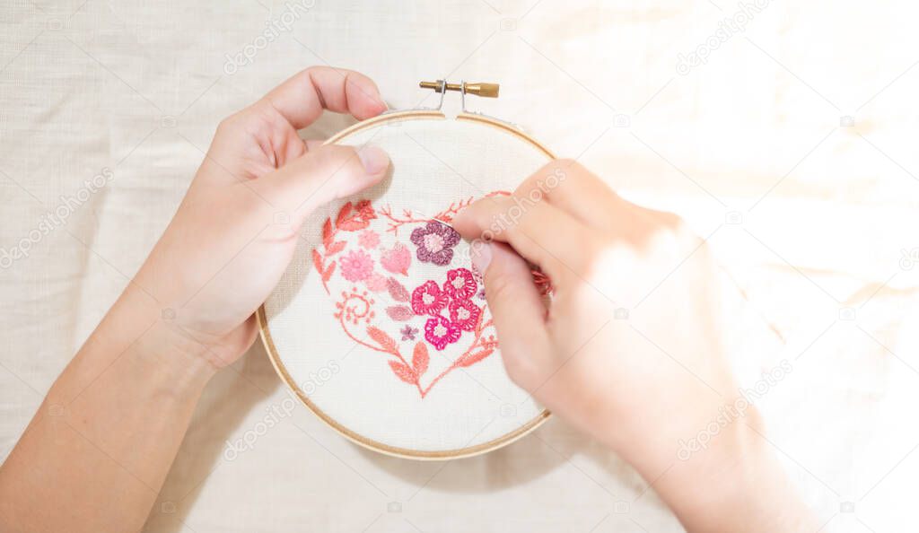 Female hand holding wood embroidery frame and needle working on flower pattern stitching in a process of handiwork.  Enjoying leisure time on weekends.