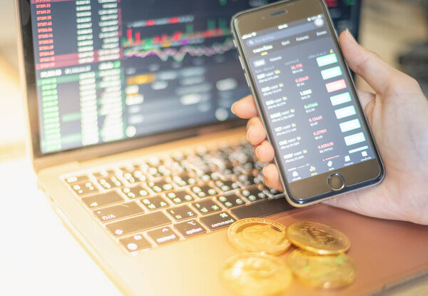 Бизнес-холдинг смартфона для инвесторов, торгующих криптовалютной монетой на ноутбуке с дисплеем и указывающих на представленные данные и сделки на фондовой бирже.